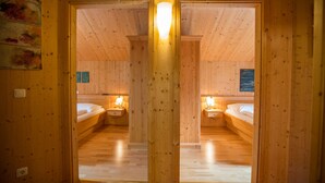 Une cabane en bois avec deux chambres, chacune équipée d’un lit simple et d’une table de chevet, ainsi que d’un luminaire central.