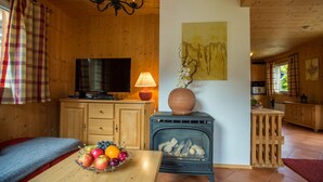 L’intérieur chaleureux d’un chalet avec une télévision, une cheminée et un panier de fruits posé sur une table en bois.