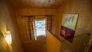 Un intérieur en bois avec un escalier, une fenêtre avec des rideaux et deux tableaux accrochés au mur.
