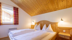 Ein Schlafzimmer mit Holzboden, einem großen Bett mit weißer Bettwäsche, zwei Nachttischen mit Lampen und einem Fenster mit Vorhängen.