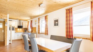 Eine moderne Küche mit weißen Schränken, einer Holzbalkendecke und einem Essbereich mit weißem Tisch und grauen Stühlen.