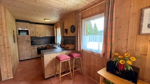 A wooden cabin interior with a kitchen, bar stools, a clock, and a window with curtains. - Chalet # 75 with 3 BR for up to 6 people (Annaberg)