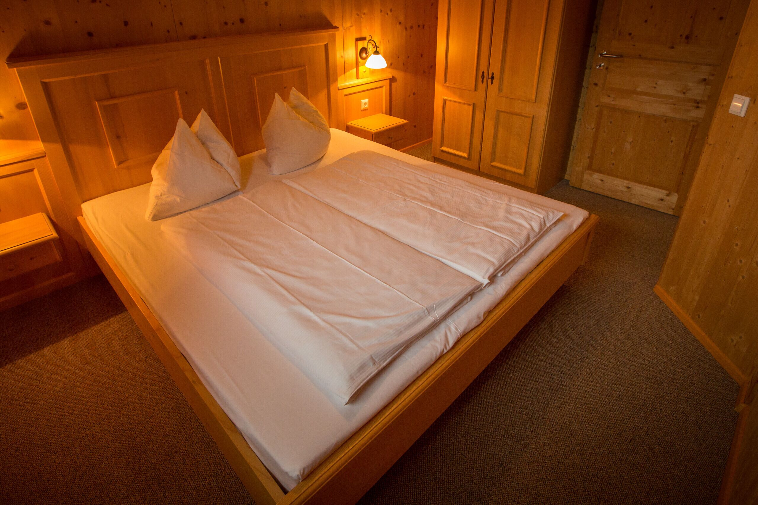 A neatly made bed with pillows, a bedside lamp, and wooden furniture in a room with a warm ambiance.