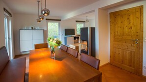 A modern dining area with a wooden table, chairs, and a vase of flowers. There is a television and a fireplace in the background. - Chalet # 21 with 3 BR for up to 6 people (Annaberg)