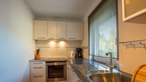 A compact kitchen with white cabinets, a stainless steel sink, and a window with blinds. - Chalet # 21 with 3 BR for up to 6 people (Annaberg)