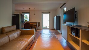 A modern living room with a leather sofa, a flat-screen TV mounted on a wooden cabinet, and a dining area with a table and chairs. - Chalet # 21 with 3 BR for up to 6 people (Annaberg)