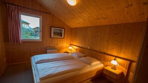 Ein Zimmer mit Holzboden, einem Bett, zwei Nachttischen mit Lampen, einem Fenster mit Vorhängen und einem Bilderrahmen an der Wand.