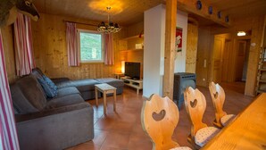 Ein gemütliches Blockhaus-Interieur mit einer Couch, einem Fernseher, Holzstühlen und einem Kamin.
