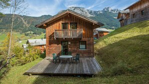 Un chalet en bois doté d’un balcon, d’une terrasse avec mobilier d’extérieur et surplombant un paysage montagneux.