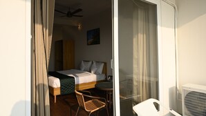 Une chambre d’hôtel avec un lit, une chaise, une petite table et un ventilateur de plafond.