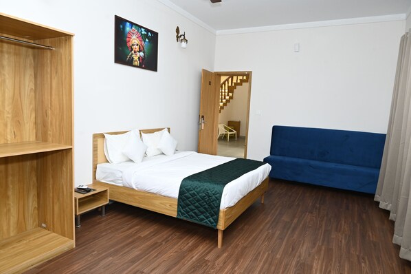 A bedroom with a wooden bed, a blue sofa, a wooden wardrobe, and a staircase leading to another room.