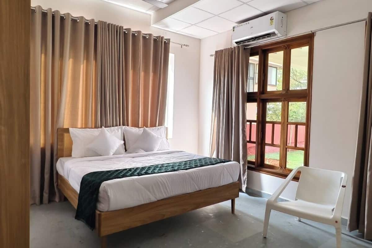A bedroom with a wooden bed, white bedding, a white chair, and a window with curtains.