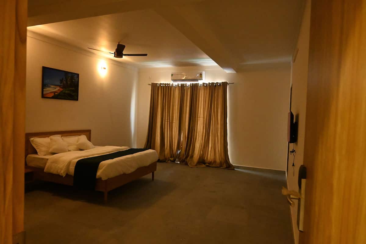 A bedroom with a bed, a ceiling fan, an air conditioning unit, and a painting on the wall.