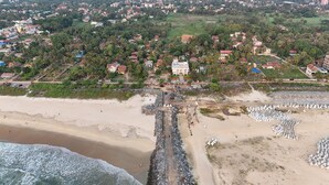 Vue aérienne d’une zone côtière comprenant une plage, un littoral rocheux et une zone résidentielle avec des maisons et de la végétation en arrière-plan.
