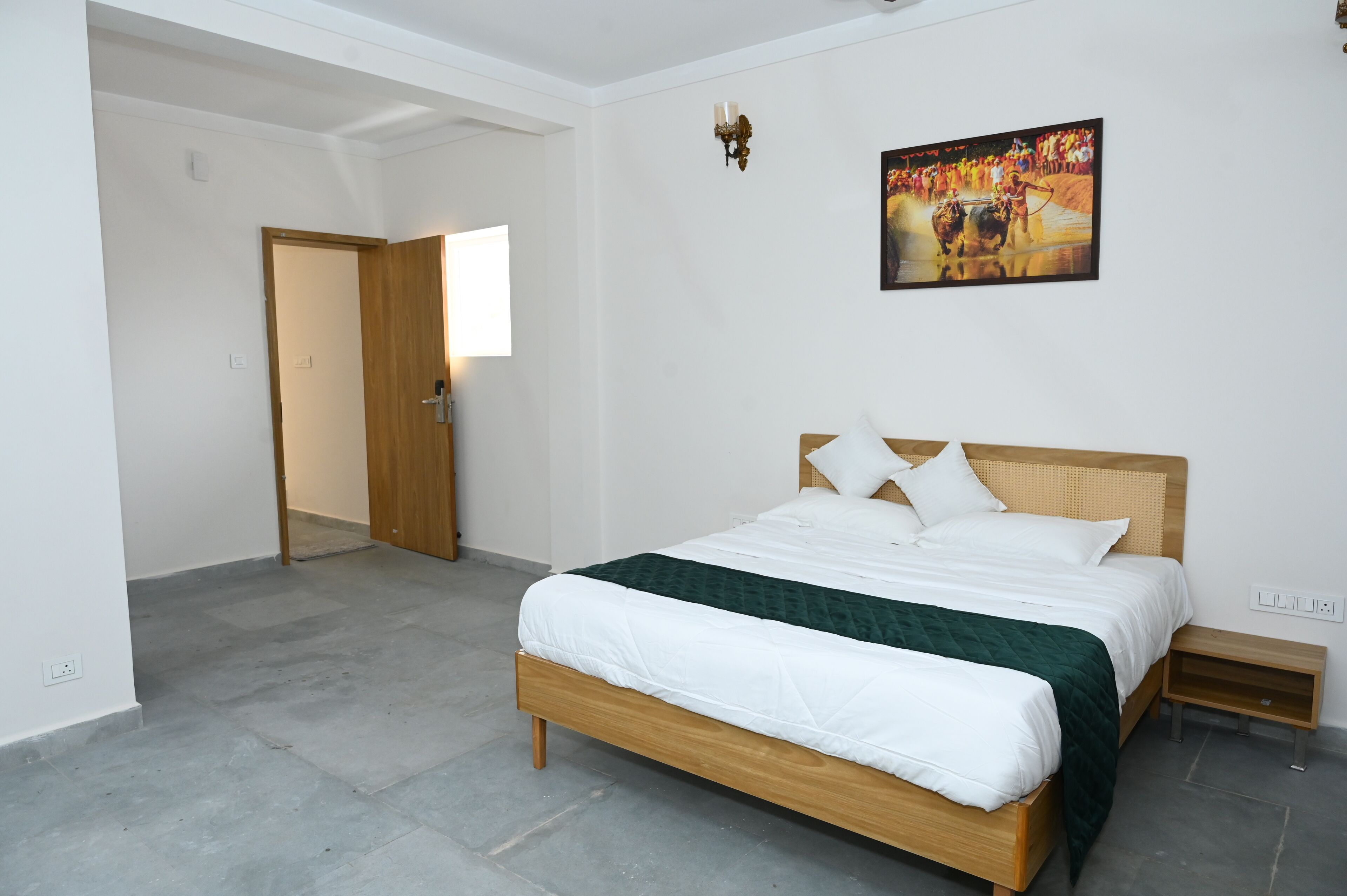 A bedroom with a wooden bed, white bedding, a green throw, a nightstand, and a wall-mounted TV displaying a bullfighting event.