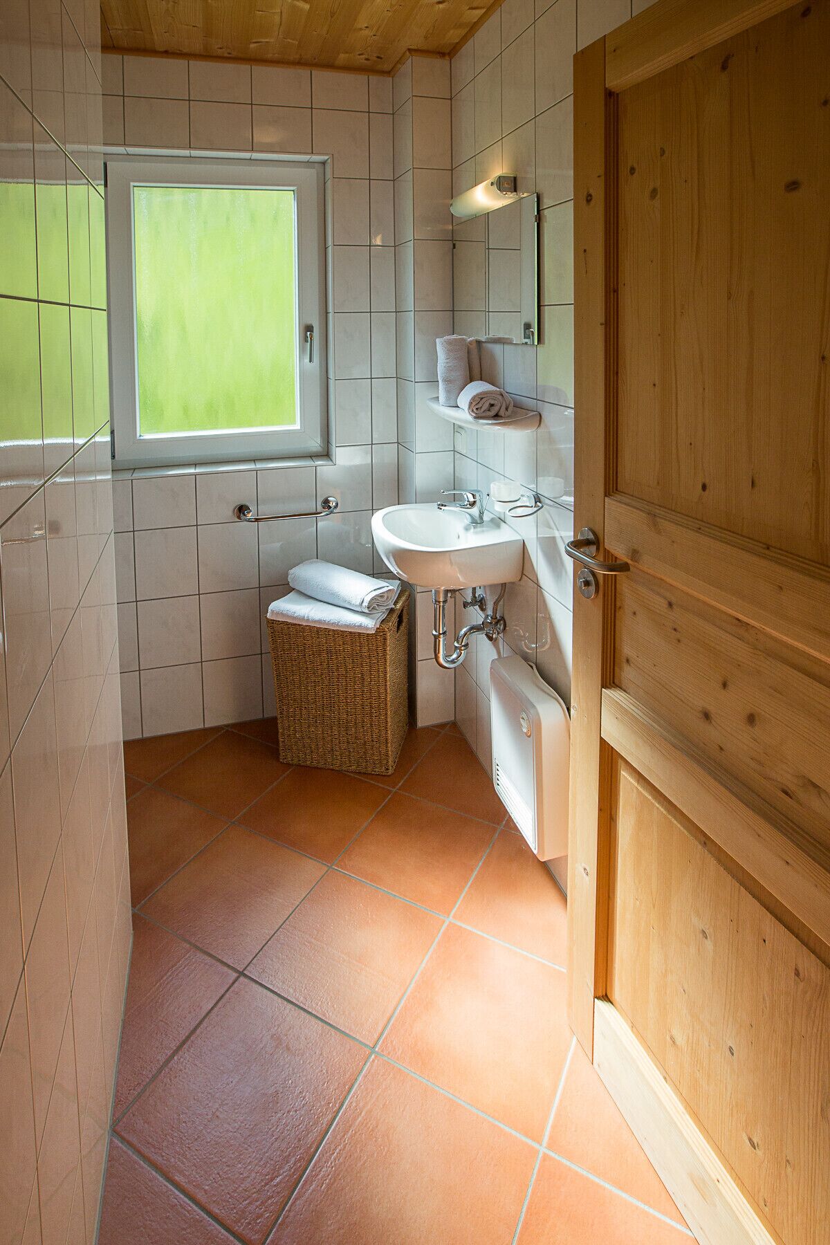 A bathroom with a window, a sink, a mirror, and a wooden door.
