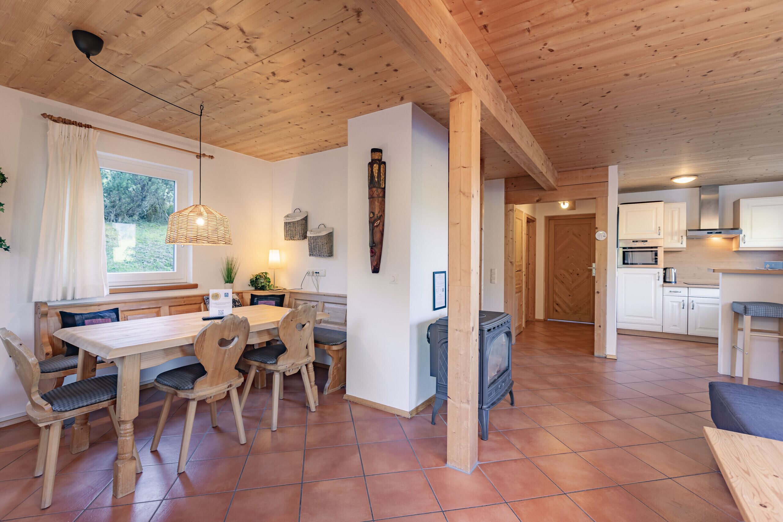 Ein Holzinterieur mit einem Esstisch, Stühlen, einer Hängelampe, einem Herd und einer Küchenzeile.