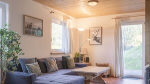 A cozy living room with a sectional sofa, a wooden coffee table, and a large window with curtains. - Chalet # 11 with 3 BR for up to 6 persons (Annaberg)