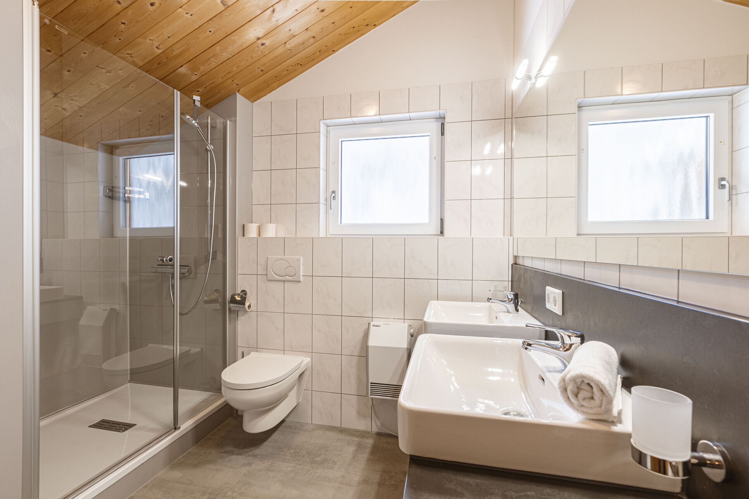 Een moderne badkamer met een glazen douchecabine, toilet, wastafel en spiegel.