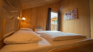 Une chambre dans un chalet en bois, avec un lit, une table de chevet, une lampe fixée au mur et une fenêtre avec des rideaux.