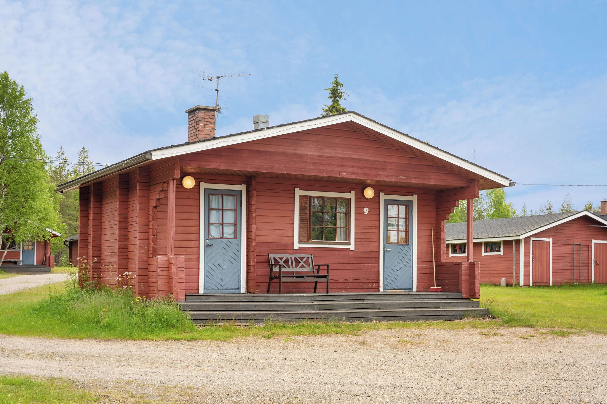 Una cabaña roja de madera con dos puertas, un banco y una chimenea.