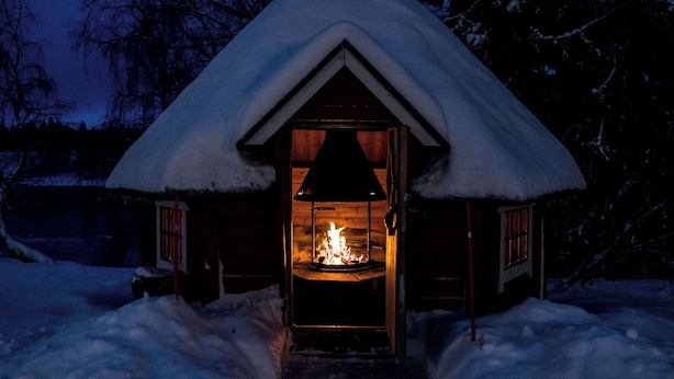 Una cabaña acogedora con techo nevado y chimenea visible.