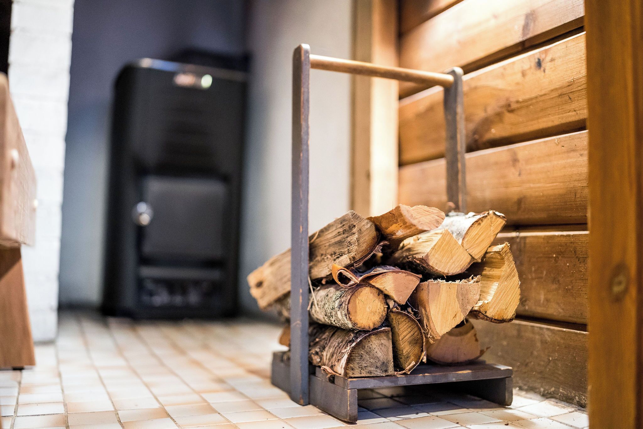 A stack of firewood on a metal rack in a room with wooden walls and a tiled floor.