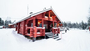 Una cabaña de troncos con un porche cubierto de nieve y escalones que conducen a la entrada.