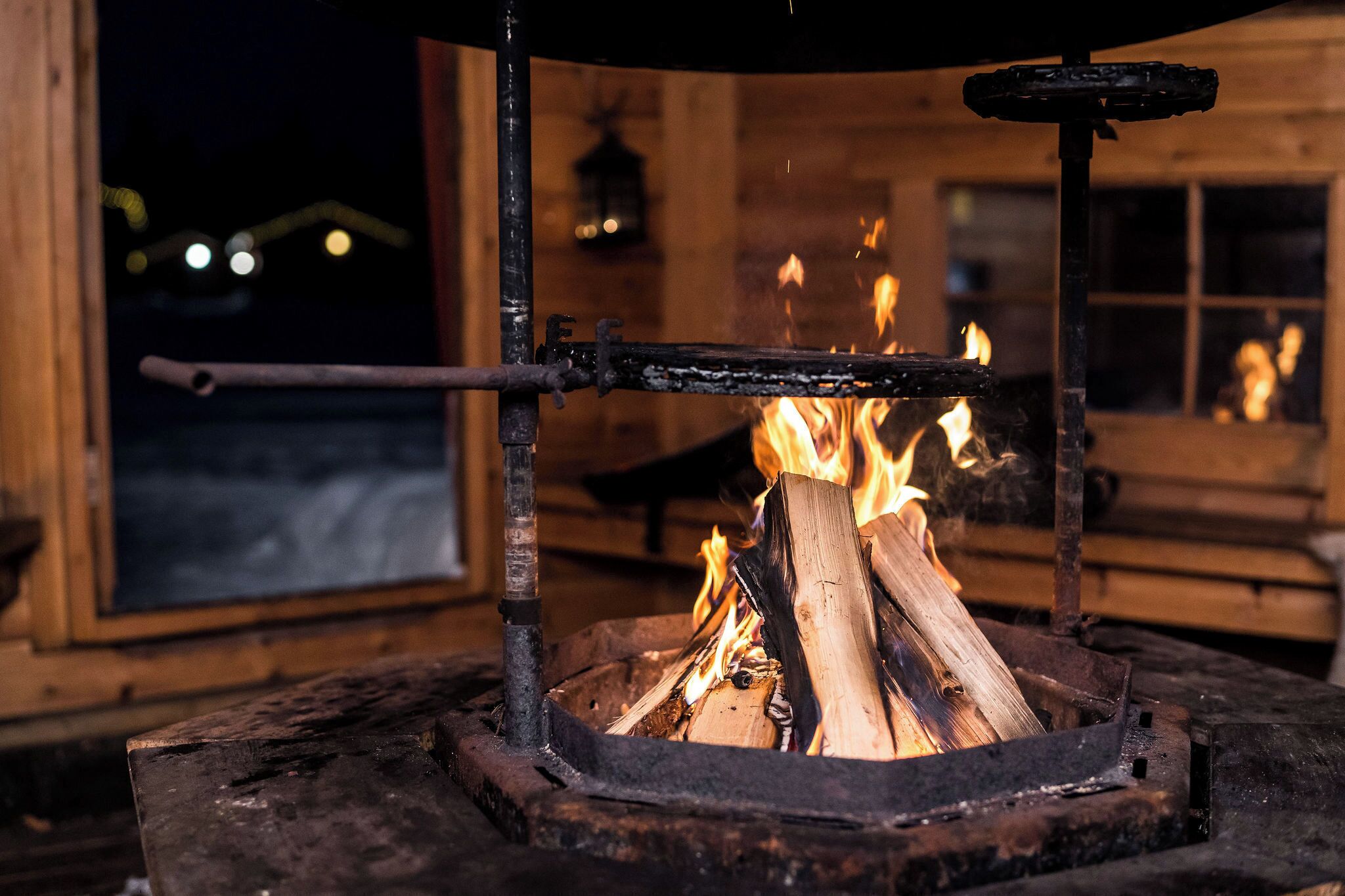 Una estufa de leña con leños ardiendo, ubicada en una cabaña de madera rústica con una ventana al fondo.