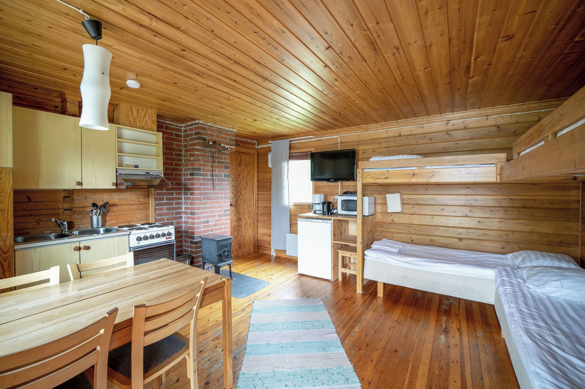 Habitació compacta amb panells de fusta, cuina, zona de menjador i un llit.
