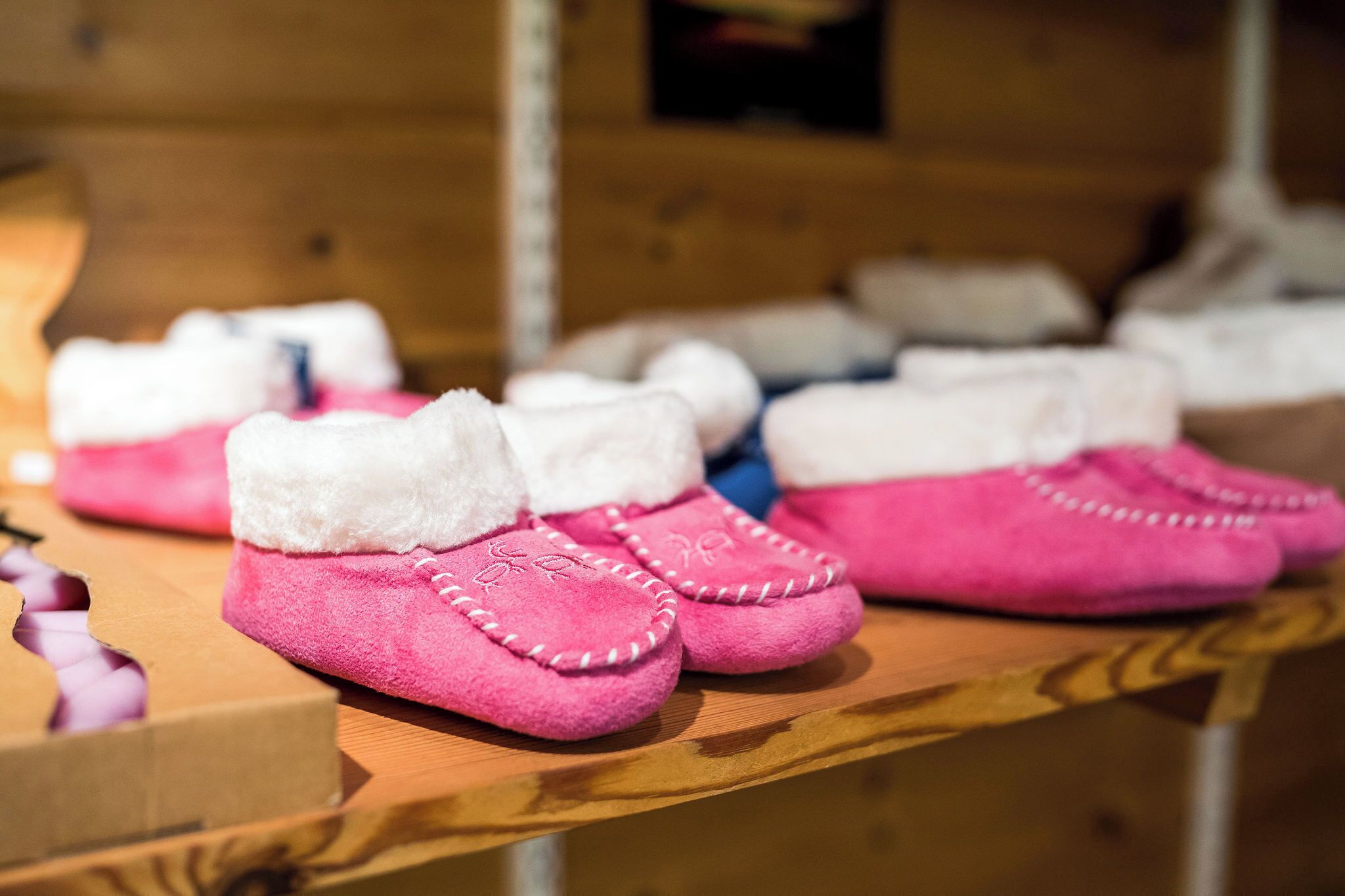 A wooden surface with pink baby shoes and a cardboard box.