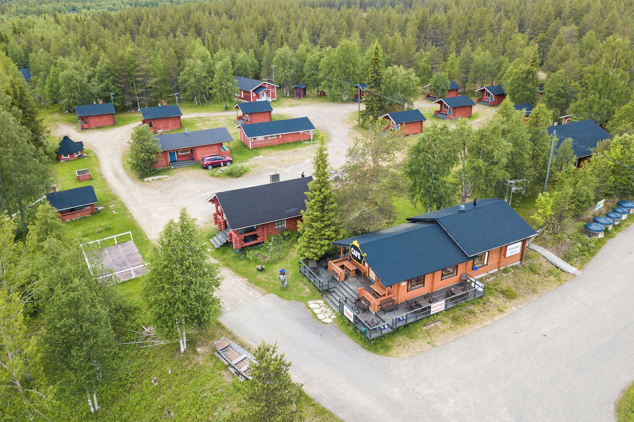 Un chalet comprenant plusieurs cabanes, un bâtiment principal avec une enseigne et une forêt environnante.