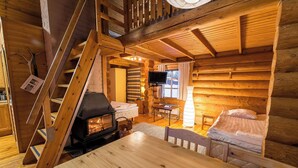 Interior acogedor de una cabaña de troncos con escalera de madera, chimenea, televisor y cama.