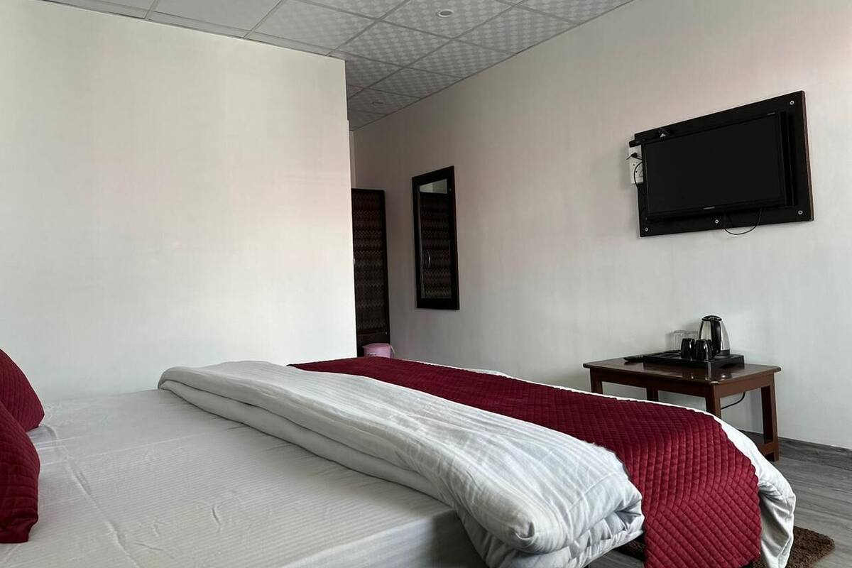 A hotel room with a bed, a TV mounted on the wall, and a small table with a kettle.
