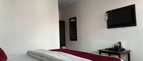 A hotel room with a bed, a TV mounted on the wall, and a small table with a kettle.