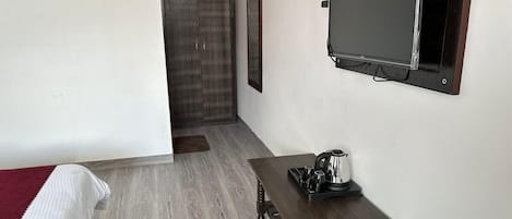 A hotel room with a bed, a small table with a kettle, a flat-screen TV, and a wardrobe.