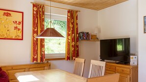 A room with a wooden table, chairs, a television, and a window with curtains. - Chalet # 43 with 3 BR for up to 6 people (Annaberg)