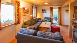 A cozy living room with a sofa, a small table with a vase, and a dining area with a chair and table. - Chalet # 43 with 3 BR for up to 6 people (Annaberg)