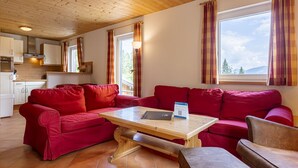 Un salón acogedor con un sofá rojo, una mesa de centro de madera y vistas al exterior a través de amplios ventanales.