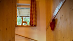 Una escalera de madera con barandilla que lleva a una habitación con ventana y una decoración de corazón rojo en la pared.