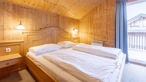 A wooden room with two beds, wooden walls, and a window with curtains.
