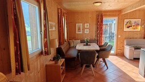 A cozy cabin interior with a wooden interior, a dining table with chairs, a sofa, and a small table with a lamp and a plant.