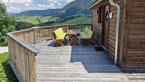 A wooden deck with two chairs and a table, overlooking a mountainous landscape.