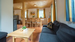 A cozy living room with a wooden ceiling, a sofa, a coffee table, and a dining area with chairs and a table.