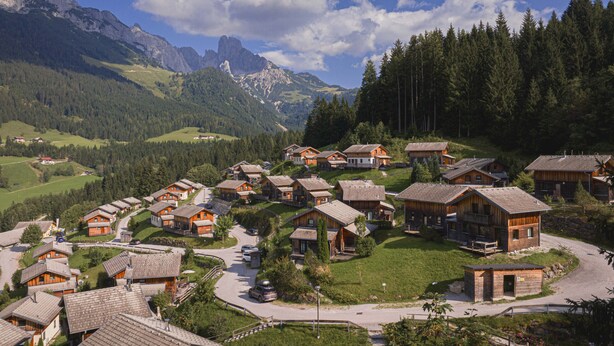 A cluster of wooden cabins with sloped roofs, surrounded by lush greenery and mountains in the background. - Chalet # 22 with 3 BR for up to 6 people (Annaberg)