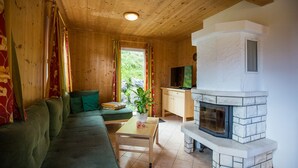 A cozy cabin interior with a wooden ceiling, a stone fireplace, a green sofa, a television, and a window with curtains. - Chalet # 22 with 3 BR for up to 6 people (Annaberg)