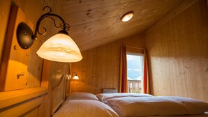 A cozy wooden cabin room with a bed, a window with curtains, and a ceiling light. - Chalet # 22 with 3 BR for up to 6 people (Annaberg)
