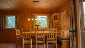 A wooden interior with a dining table, chairs, and a bench. There are windows with curtains, a hanging light fixture, and a painting on the wall. - Chalet # 65 with 3 BR for up to 6 people (Annaberg)
