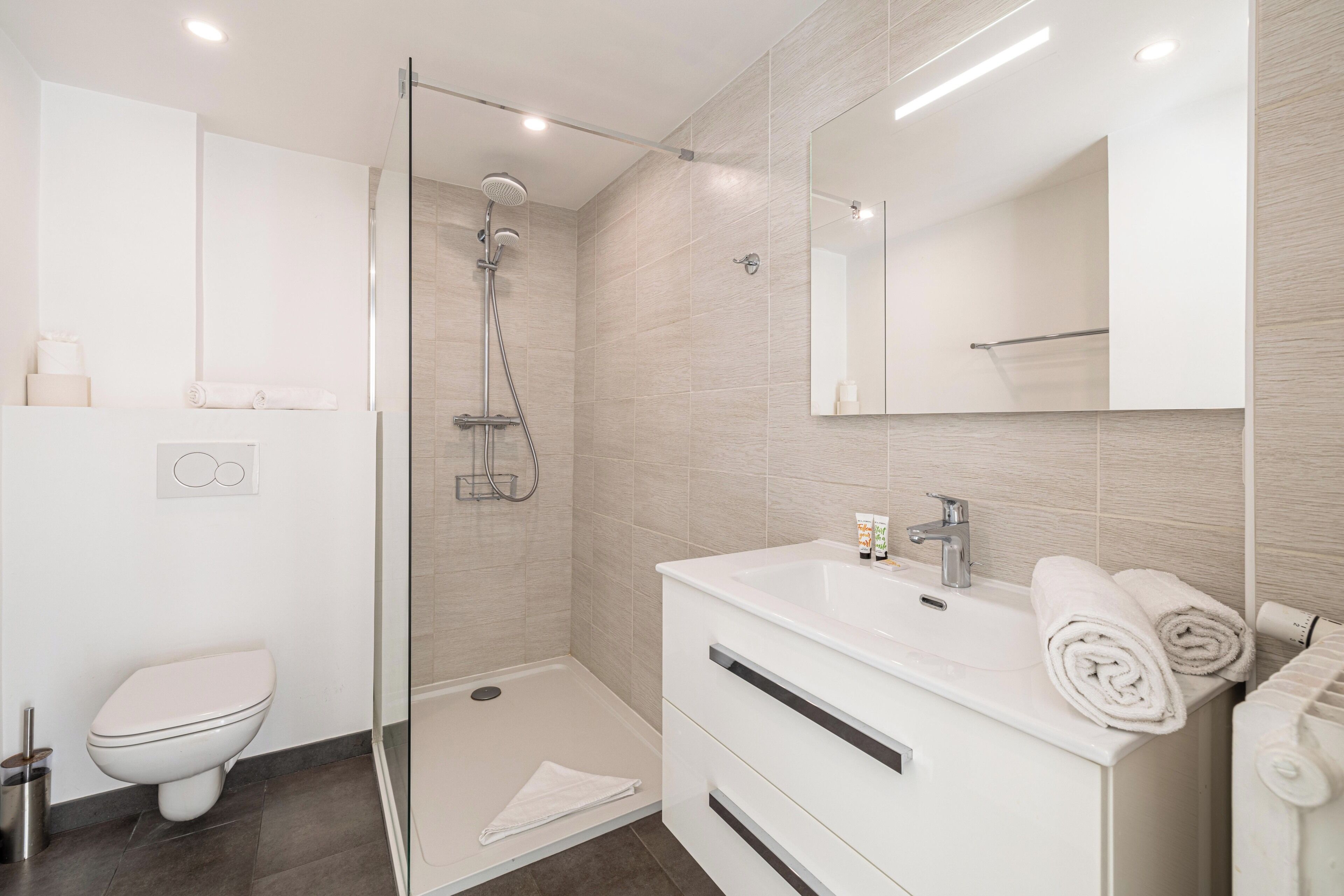 Un bagno moderno con doccia a vetro, un lavandino bianco con specchio e un water.
