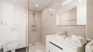 Un baño moderno con ducha de vidrio, lavamanos blanco con espejo y retrete.